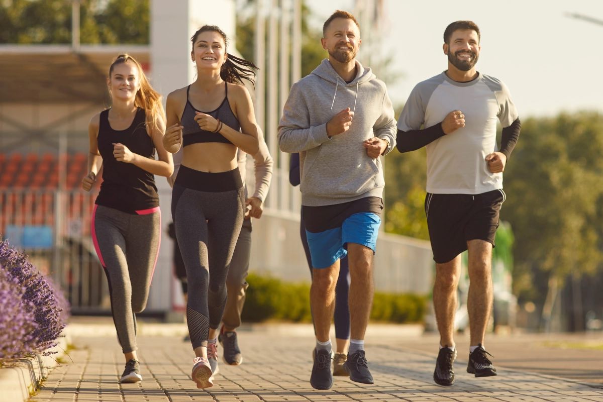 Four adults running together along a path in warm morning light